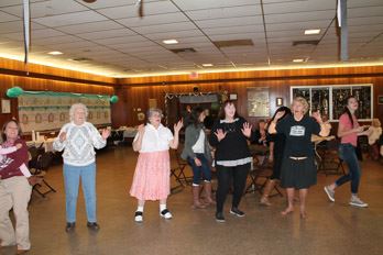 People dance in a half circle, facing inward with palms raised.